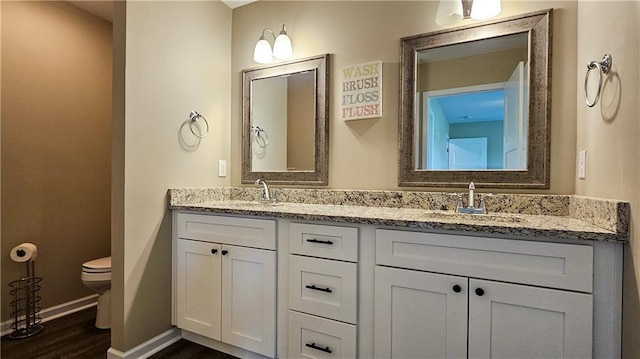 bathroom featuring toilet, double vanity, a sink, and baseboards