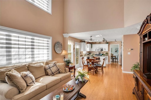 living room featuring ceiling fan, a towering ceiling, light hardwood / wood-style floors, and track lighting