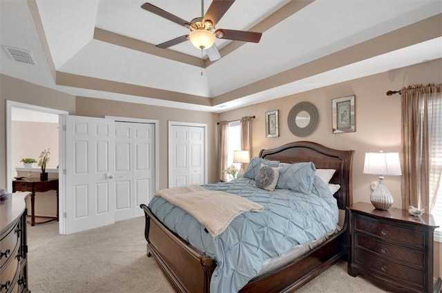 carpeted bedroom with a raised ceiling, ceiling fan, and two closets