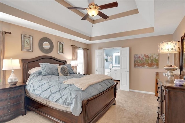 bedroom with light carpet, a raised ceiling, ensuite bath, and ceiling fan