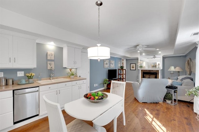 dining room with a raised ceiling, ceiling fan, sink, and light wood-type flooring