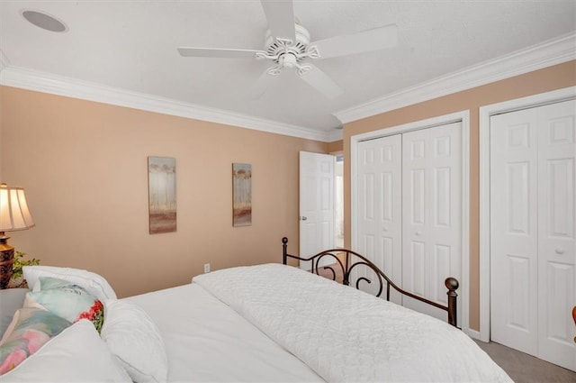 carpeted bedroom with two closets, ceiling fan, and crown molding