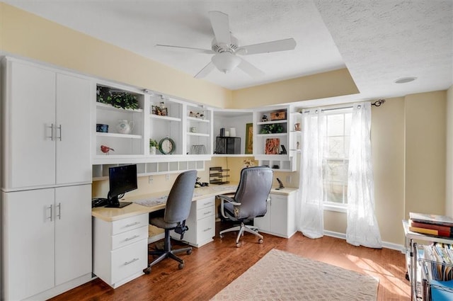 office space with ceiling fan, built in desk, wood-type flooring, and a textured ceiling