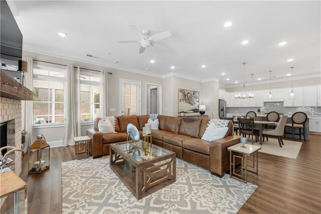 living area with ornamental molding, ceiling fan with notable chandelier, a fireplace, and wood finished floors