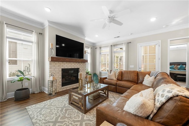 living room featuring crown molding, a brick fireplace, baseboards, wood finished floors, and a ceiling fan