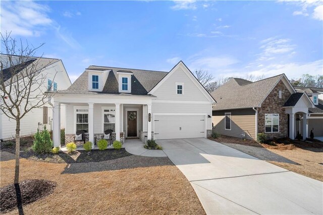 view of front of house featuring driveway, stone siding, roof with shingles, an attached garage, and a porch