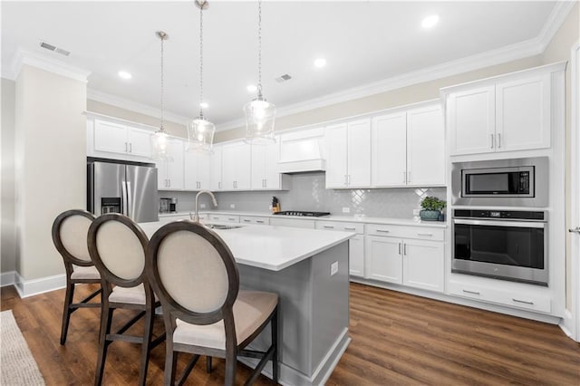 kitchen featuring visible vents, custom exhaust hood, a breakfast bar, a kitchen island with sink, and stainless steel appliances