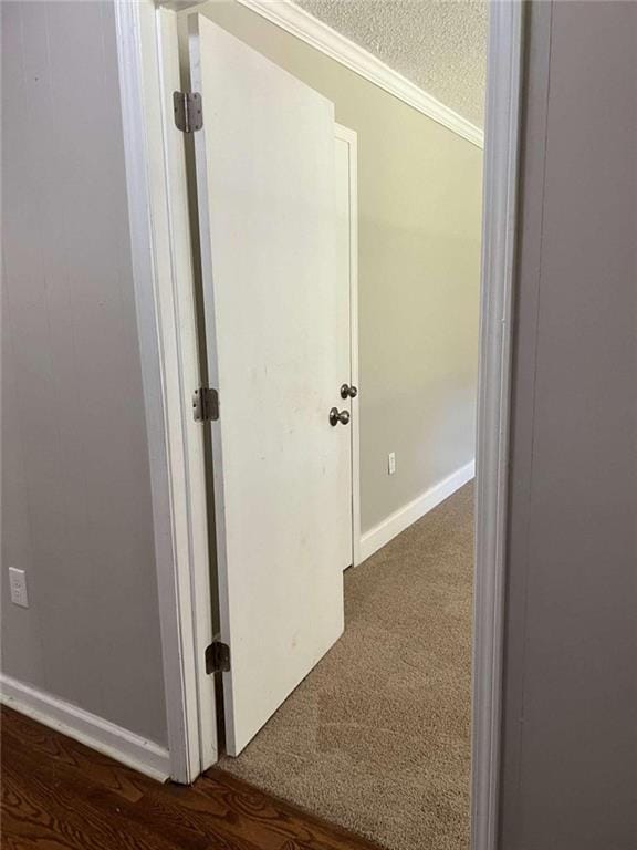 corridor with a textured ceiling, dark colored carpet, and baseboards