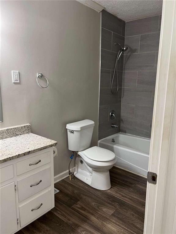 full bathroom featuring a textured ceiling, hardwood / wood-style floors, toilet, vanity, and tiled shower / bath combo