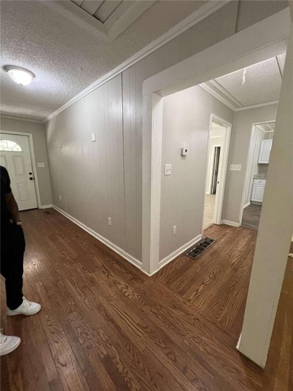 foyer featuring crown molding, visible vents, dark wood-type flooring, a textured ceiling, and baseboards