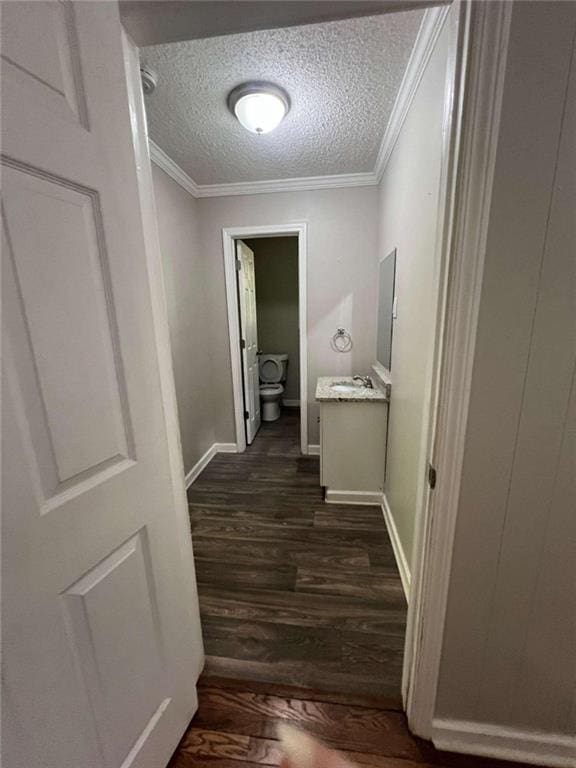 hall with a textured ceiling, ornamental molding, dark wood-type flooring, and baseboards