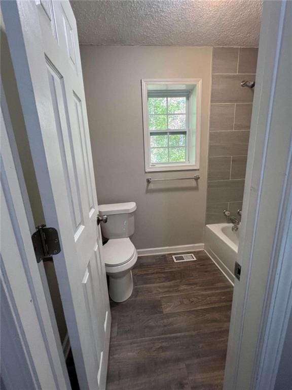 full bathroom with shower / washtub combination, toilet, a textured ceiling, wood finished floors, and baseboards