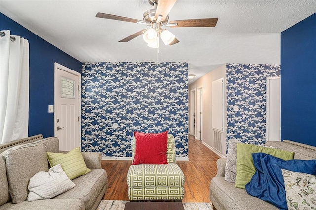 living room with a ceiling fan, wood finished floors, wallpapered walls, a textured ceiling, and baseboards