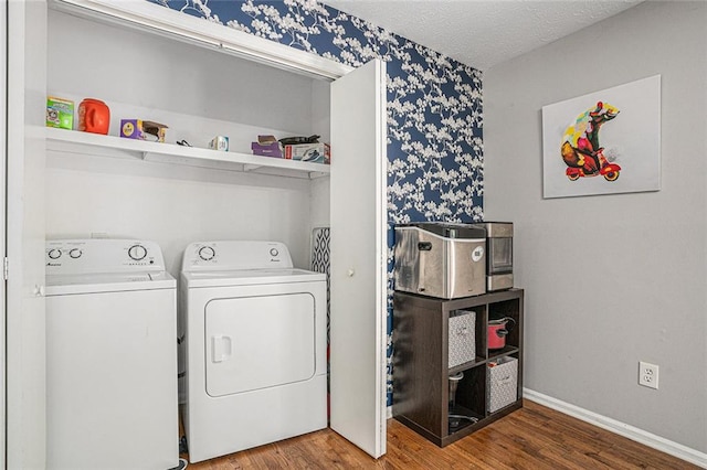 laundry room with washing machine and clothes dryer, wallpapered walls, wood finished floors, baseboards, and a textured ceiling