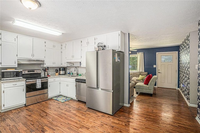 kitchen with appliances with stainless steel finishes, under cabinet range hood, a textured ceiling, wood finished floors, and a sink