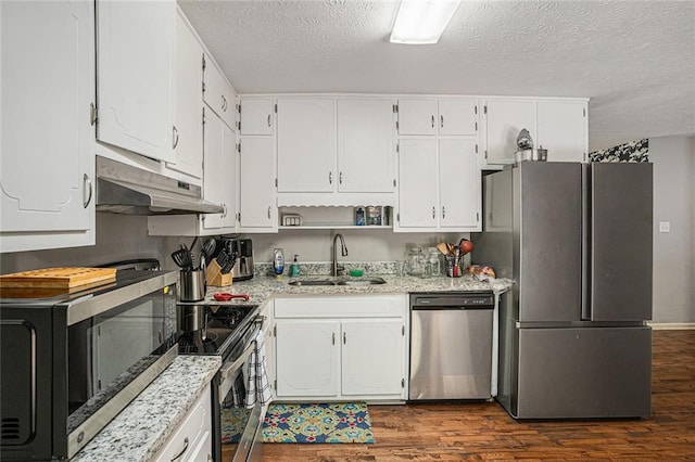 kitchen with appliances with stainless steel finishes, a sink, under cabinet range hood, dark wood-style flooring, and a textured ceiling