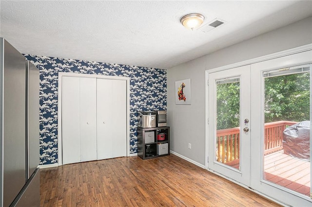 bedroom featuring wallpapered walls, wood finished floors, access to exterior, freestanding refrigerator, and french doors