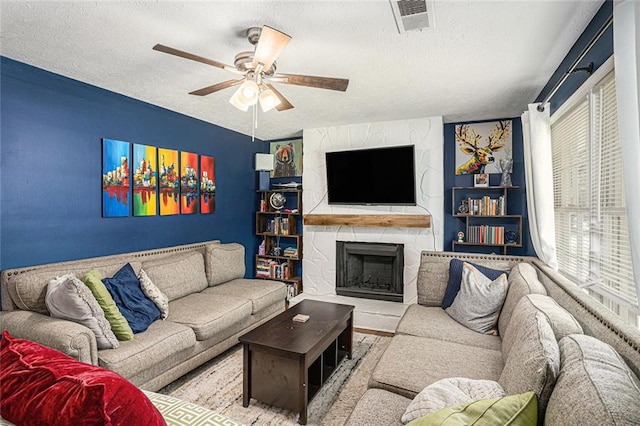 living room with a textured ceiling, a ceiling fan, a large fireplace, and built in features