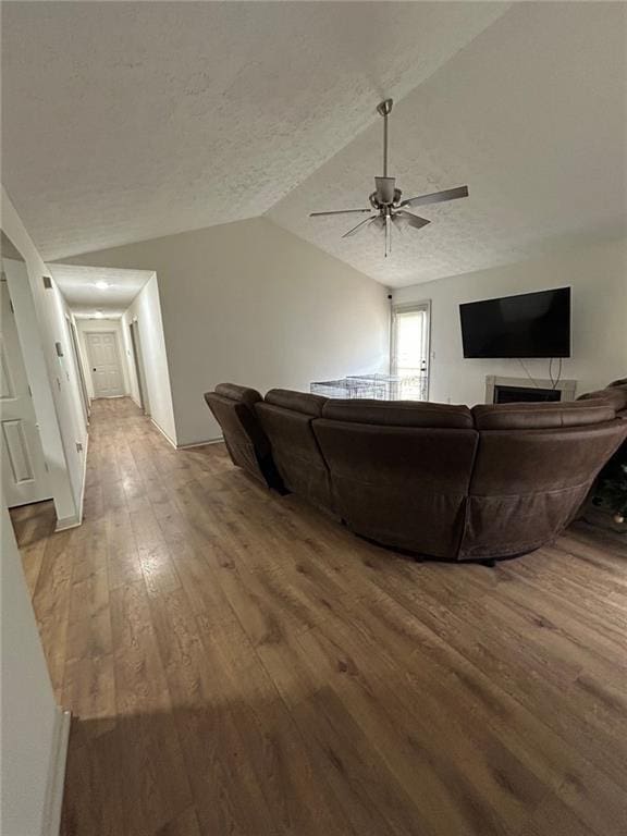 living room featuring hardwood / wood-style floors, vaulted ceiling, a textured ceiling, and ceiling fan