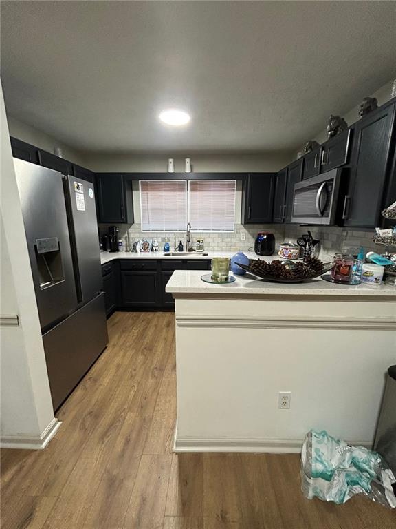 kitchen featuring appliances with stainless steel finishes, sink, decorative backsplash, and light wood-type flooring