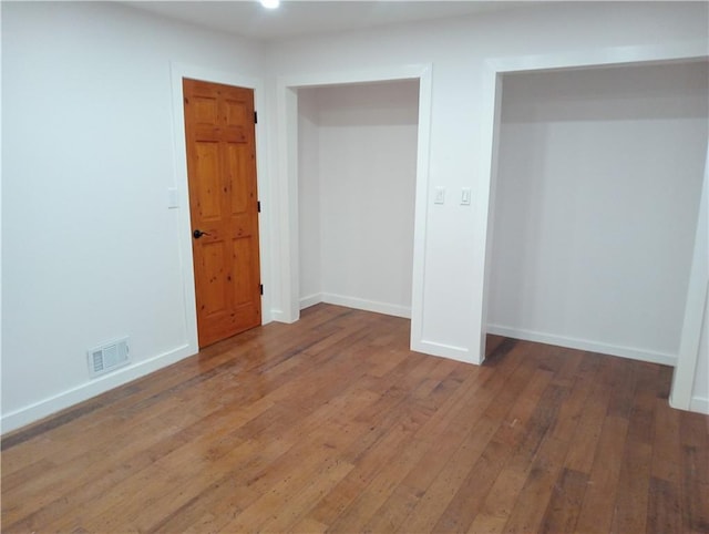 unfurnished bedroom with wood-type flooring, visible vents, and baseboards