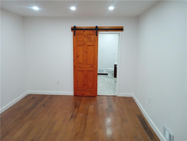 unfurnished room with a barn door, visible vents, baseboards, hardwood / wood-style flooring, and recessed lighting