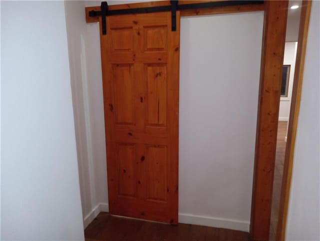 hall with dark wood-type flooring, baseboards, and a barn door