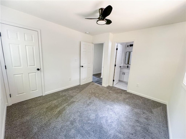 unfurnished bedroom featuring connected bathroom, a closet, dark carpet, and ceiling fan