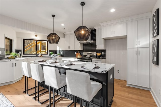 kitchen with electric stove, white cabinetry, hanging light fixtures, a center island, and wall chimney exhaust hood