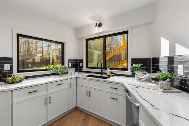 kitchen with white cabinetry, sink, decorative backsplash, stainless steel dishwasher, and light stone counters