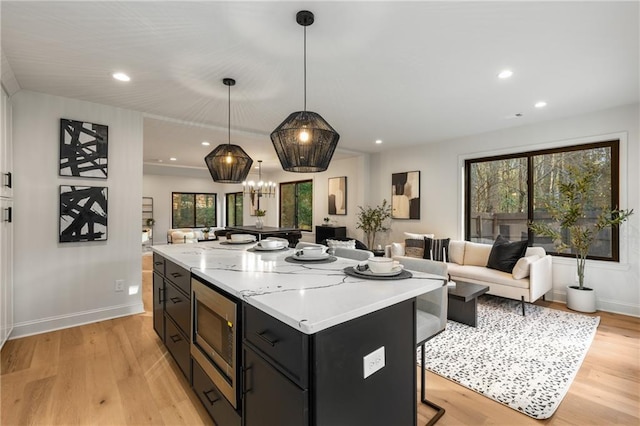 kitchen with pendant lighting, stainless steel microwave, a kitchen breakfast bar, a center island, and light hardwood / wood-style floors