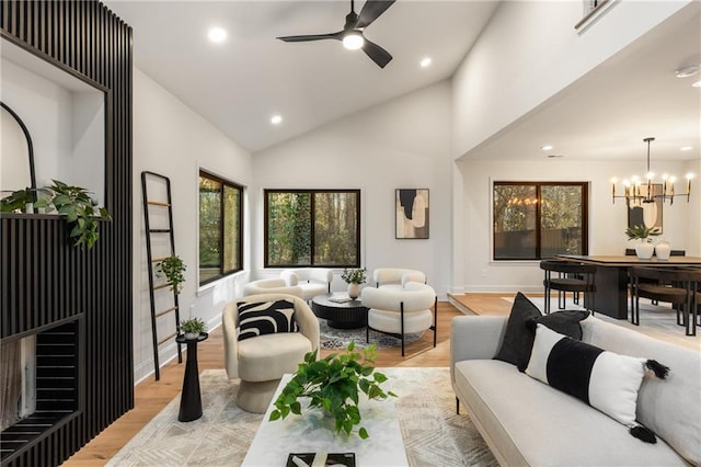 living room with ceiling fan with notable chandelier, high vaulted ceiling, a fireplace, and light hardwood / wood-style floors