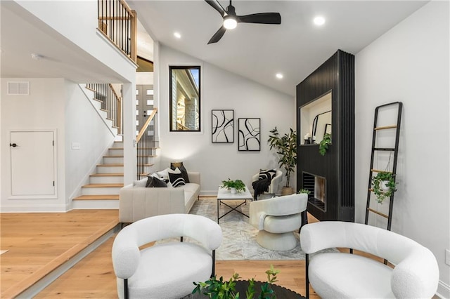 living room with hardwood / wood-style flooring, ceiling fan, lofted ceiling, and a large fireplace