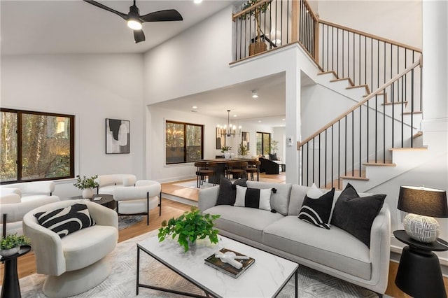 living room with wood-type flooring, ceiling fan with notable chandelier, and a high ceiling