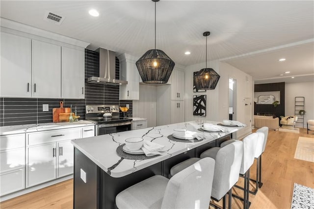 kitchen with wall chimney range hood, white cabinetry, a center island, decorative light fixtures, and stainless steel electric stove