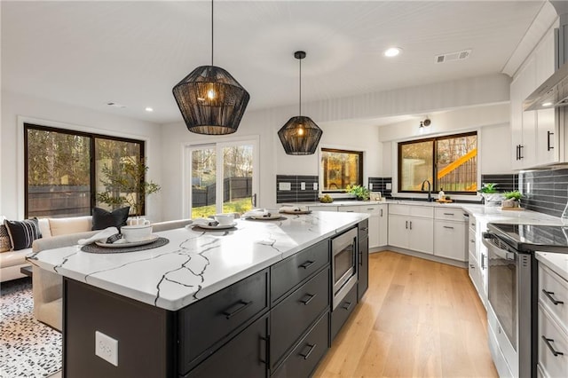 kitchen with light stone counters, appliances with stainless steel finishes, a kitchen island, pendant lighting, and white cabinets