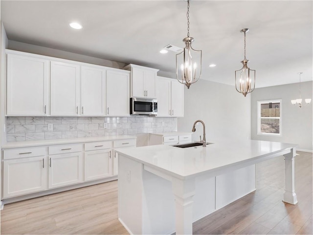 kitchen featuring pendant lighting, sink, white cabinets, backsplash, and a center island with sink