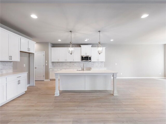 kitchen featuring sink, a kitchen island with sink, an inviting chandelier, white cabinets, and decorative light fixtures