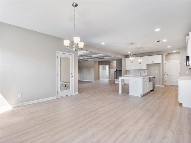 kitchen featuring pendant lighting, tasteful backsplash, sink, white cabinets, and a center island with sink