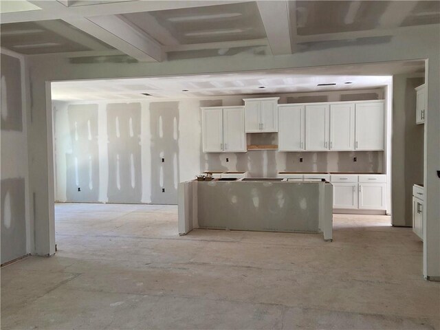 kitchen featuring sink, hanging light fixtures, beam ceiling, an island with sink, and white cabinets