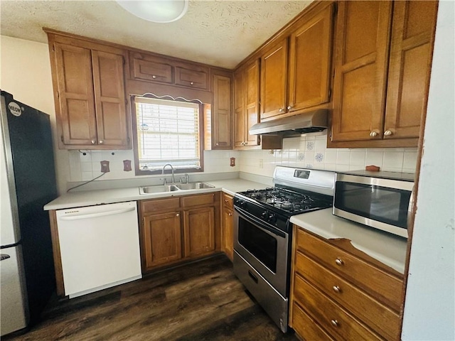 kitchen with a sink, dark wood-type flooring, appliances with stainless steel finishes, under cabinet range hood, and brown cabinets