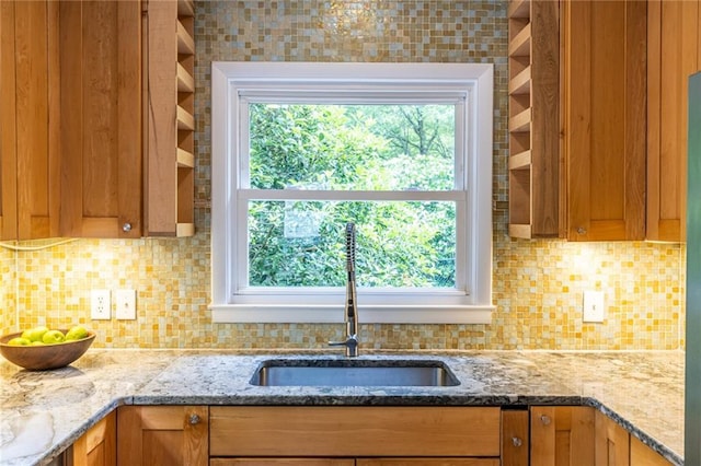 kitchen with a sink, open shelves, light stone countertops, and backsplash