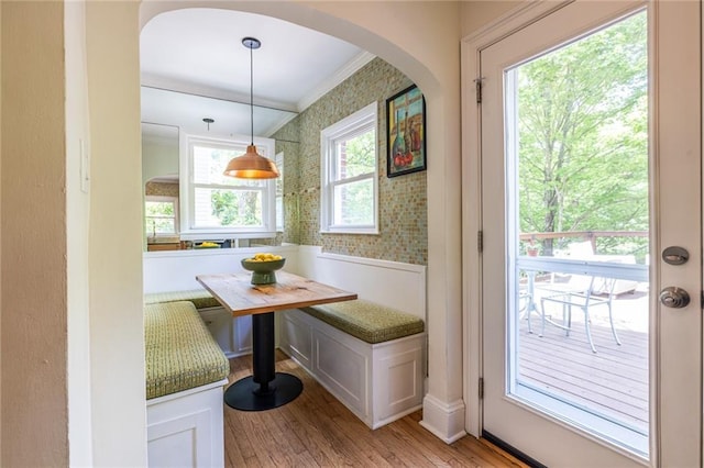 doorway to outside featuring ornamental molding, light wood-type flooring, arched walkways, and wallpapered walls