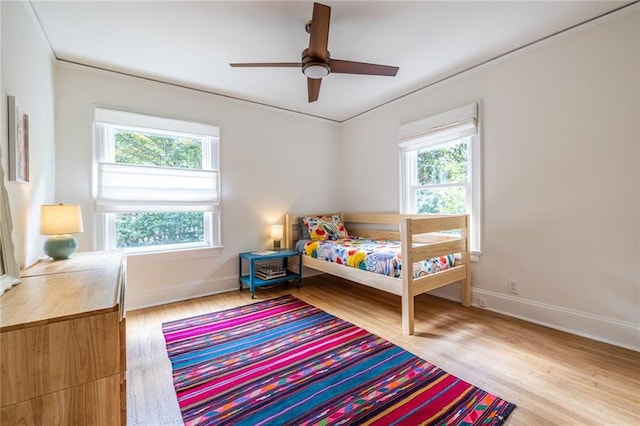 bedroom with multiple windows, ornamental molding, wood finished floors, and baseboards
