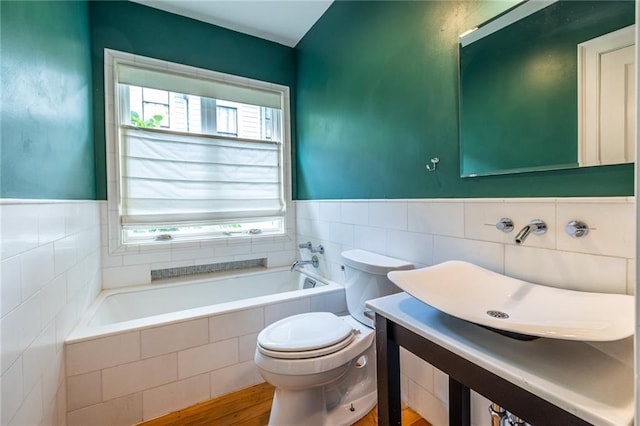 bathroom with tile walls, a garden tub, toilet, a wainscoted wall, and a sink