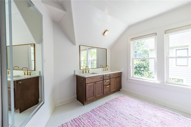 bathroom with double vanity, vaulted ceiling, plenty of natural light, and baseboards