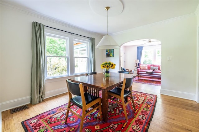 dining space featuring arched walkways, crown molding, baseboards, and light wood-style flooring