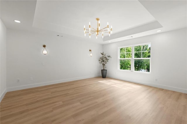 spare room with a tray ceiling, a chandelier, recessed lighting, light wood-style flooring, and baseboards