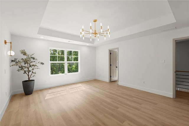 spare room featuring a tray ceiling, light wood-style flooring, a chandelier, baseboards, and recessed lighting