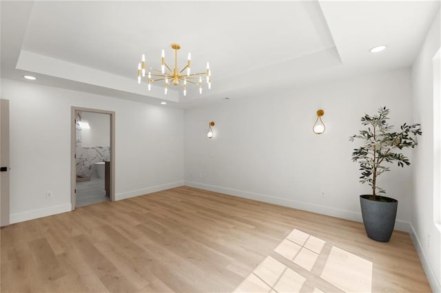 unfurnished room with a raised ceiling, a chandelier, light wood-style flooring, recessed lighting, and baseboards